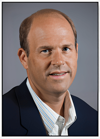 Professional portrait of a man in a blazer and plaid shirt